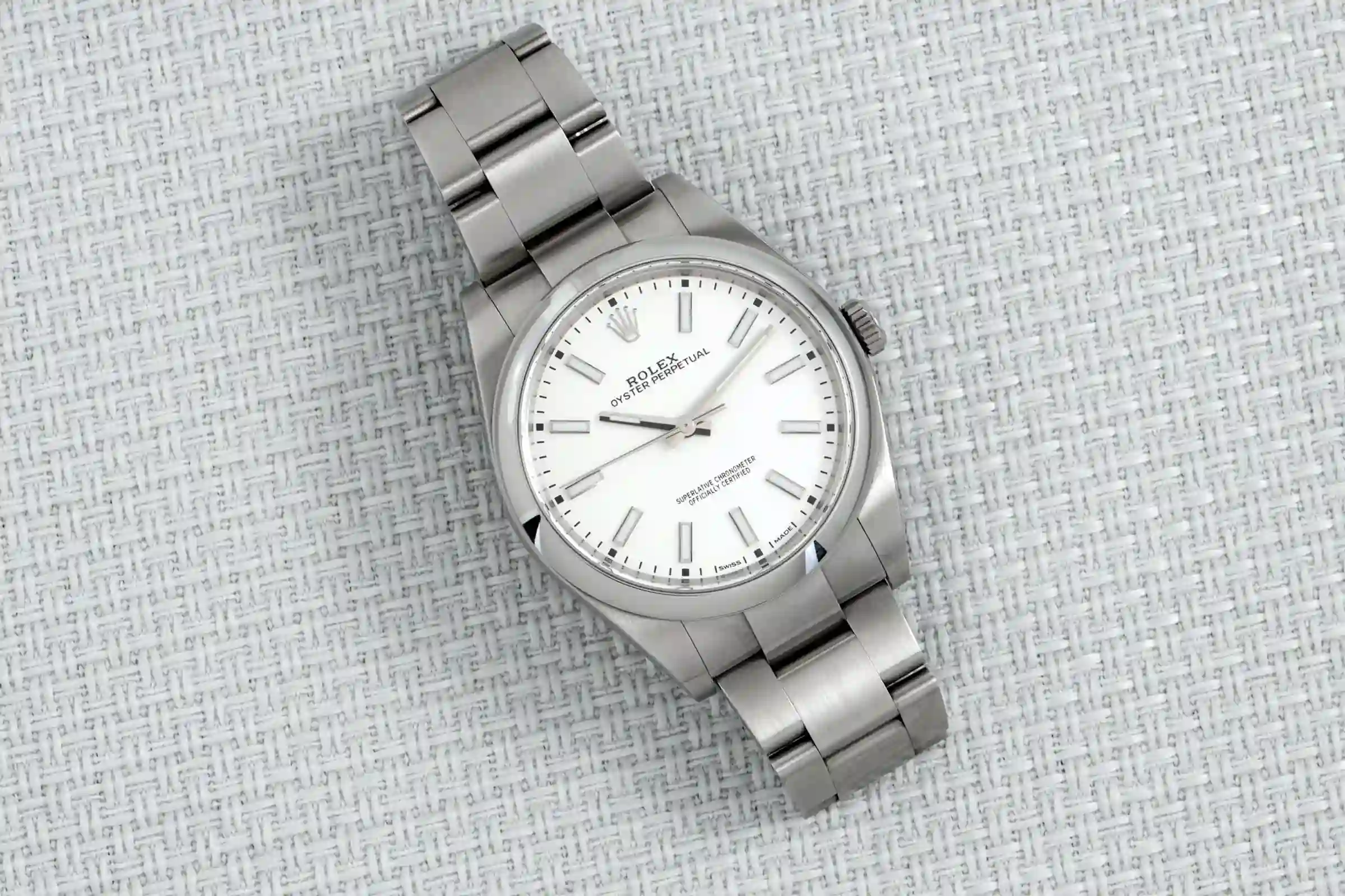 Reloj Rolex Oyster Perpetual 38 de acero con esfera blanca y brazalete metálico sobre fondo texturizado claro.